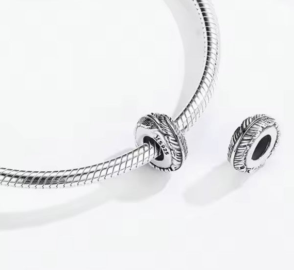 Zilveren spacer in veer-motief die soepel over de armband glijdt en vastklemt op de metalen uiteinden.
